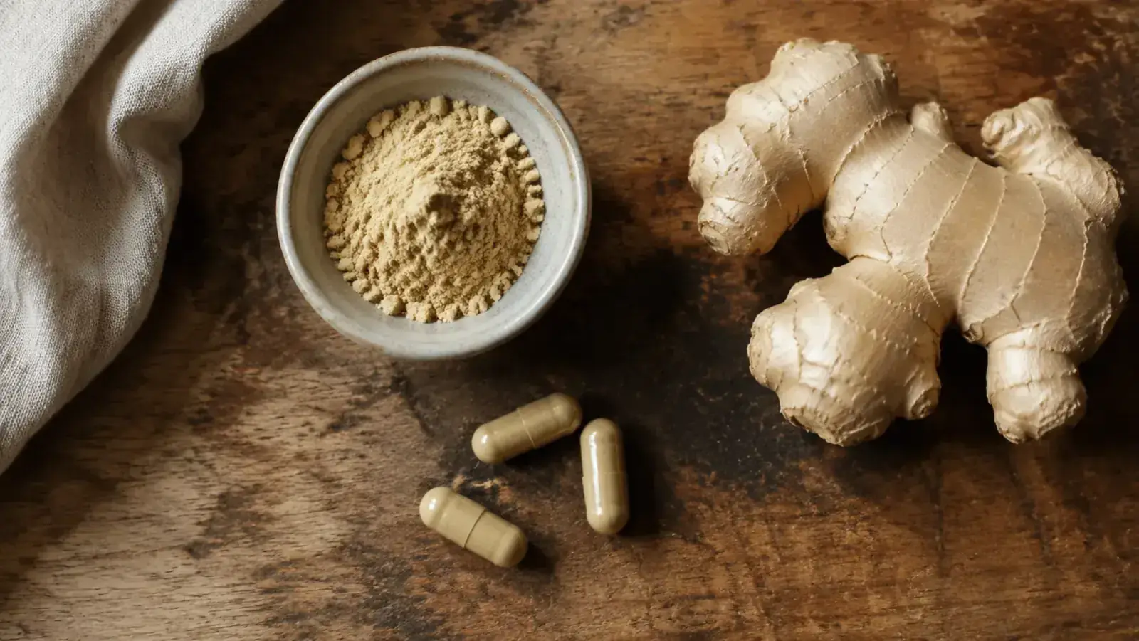 Ginger root capsules arranged next to fresh ginger root on a wooden cutting board in a home kitchen